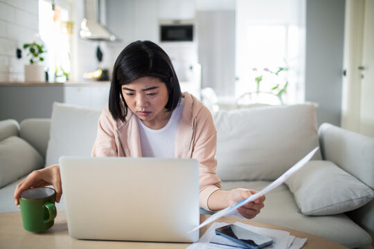 Young woman thinking about bills at home with laptop