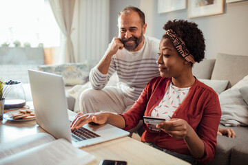 Diverse middle aged couple using laptop for online shopping at home