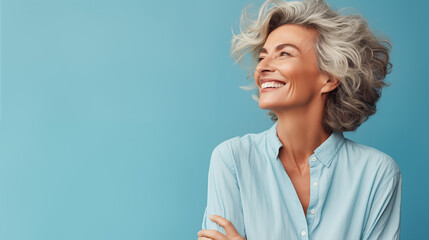 Against a pastel blue canvas, a mature woman exudes carefree vibes in a waist-up portrait. Her relaxed demeanor and joyful expression convey a sense of freedom and happiness