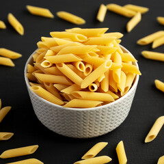 Organic Dry Penne Pasta in a Bowl on a black background, side view.