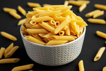 Organic Dry Penne Pasta in a Bowl on a black background, side view.