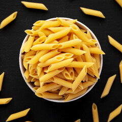 Organic Dry Penne Pasta in a Bowl on a black background, top view.