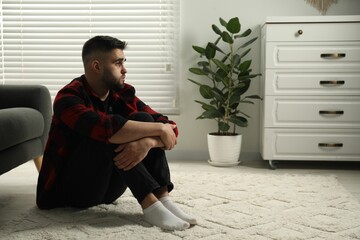 Sad man sitting on floor at home. Space for text