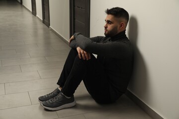 Sad man sitting on floor in hall. Space for text