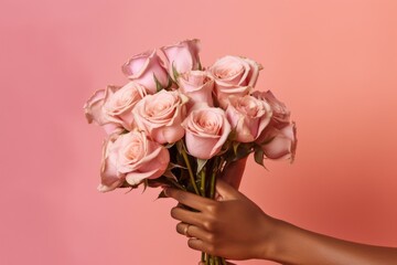 close up of an African American woman's hand tenderly holding a bouquet of roses, set against a soft pink backdrop