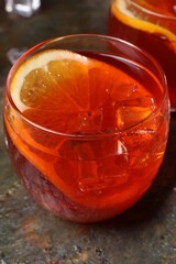 Aperol spritz cocktail, ice cubes and orange slice in glass on grey textured table, closeup