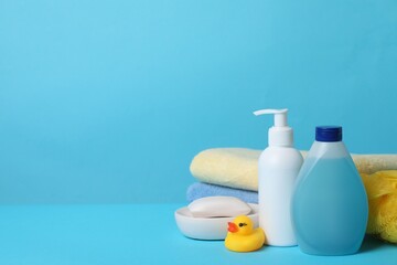 Fototapeta na wymiar Baby cosmetic products, bath duck, sponge and towels on light blue background. Space for text