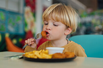 happy boy with blond hair eats fries and nuggets in restaurant