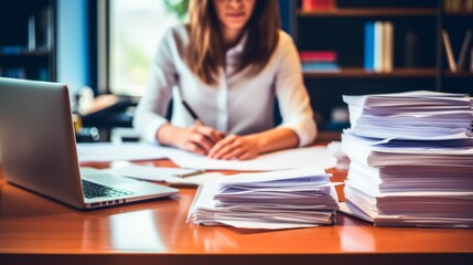 young business woman working in the office desk with piles of paper and a laptop