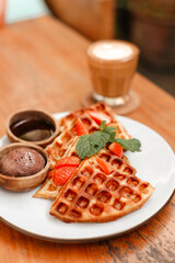 Waffles with strawberries on a white plate for breakfast. Delicious waffles with berries, chocolate and coffee. Fragrant Fresh Breakfast Pastries