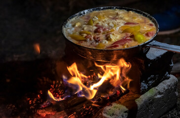 cooking scrambled eggs with vegetables over a fire in an aluminum frying pan
