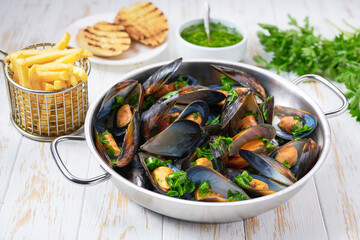 traditional belgian dish steamed mussels with french fries on a white wooden table.