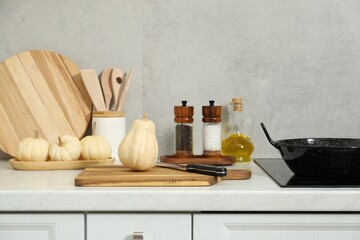 Fototapeta na wymiar Wooden cutting boards, other cooking utensils and pumpkins on white countertop in kitchen