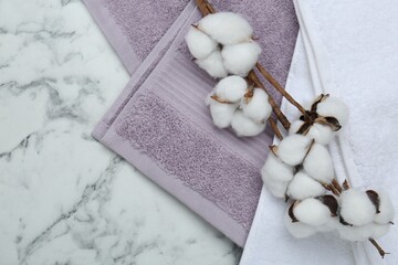 Different terry towels and cotton flowers on white marble table, flat lay. Space for text