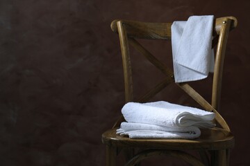 White terry towels on wooden chair against brown background. Space for text