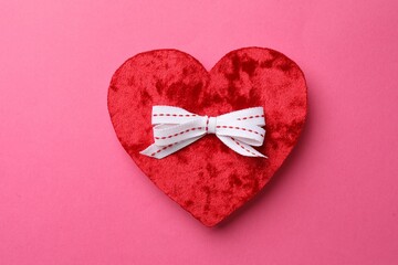 Red textile heart with white bow on pink background, top view