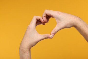 Man showing heart gesture with hands on golden background, closeup