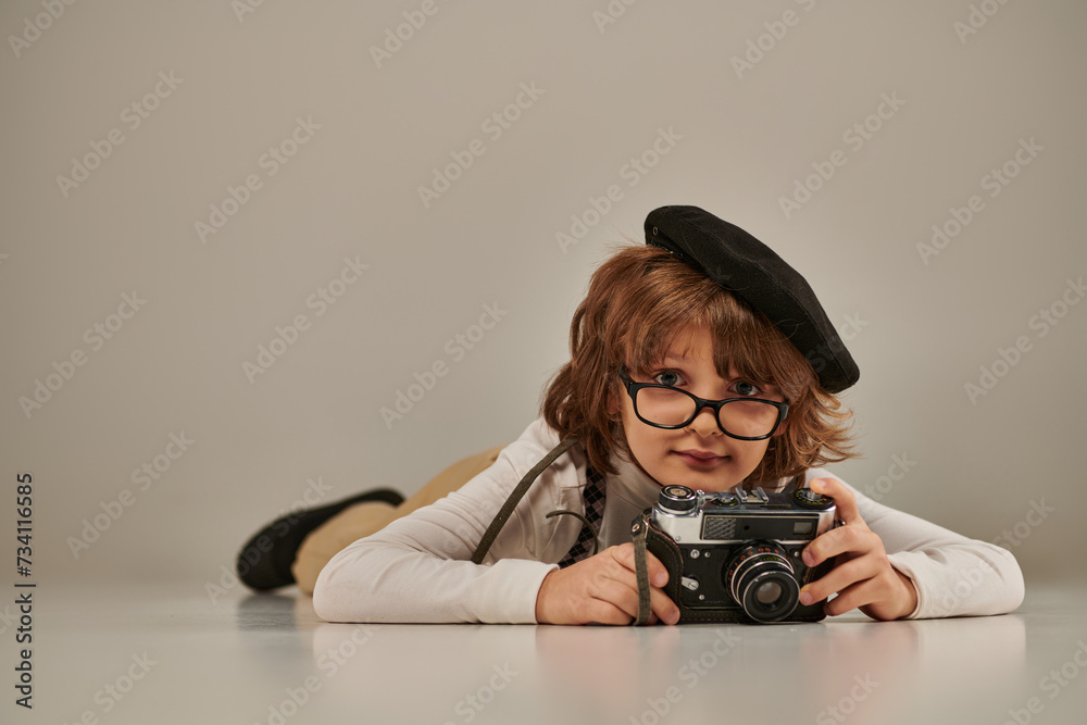 Wall mural happy young photographer in beret and suspenders taking photo on retro camera and lying on floor