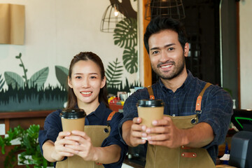 Multiracial man businessman cafe owner small business holding paper coffee cup Asian girlfriend both looking camera Inside the coffee shop Behind there is coffee machine in minimalist style shop