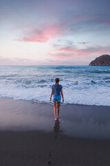 A young girl walks along the beach to the sea during sunset