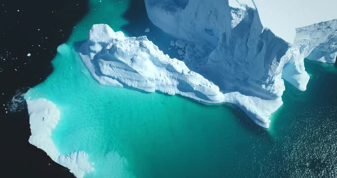 Melting snow covered glacier in blue water aerial top view. Nature beauty towering floating iceberg. Polar winter landscape. Ecology, melting ice, climate change, global warming background. Drone shot