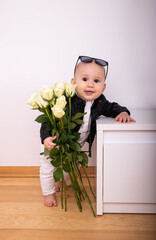 Portrait of child holds roses in his hands with in a white to stand on their feet holding a white bedside table on the background of a white wall greeting card for March 8 birthday Valentine's Day