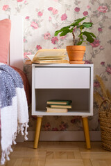 Bedside table in bedroom with floral wallpaper.