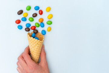 A hand holding an empty waffle cone with scattered multicolored round candies, dragees. A fun holiday