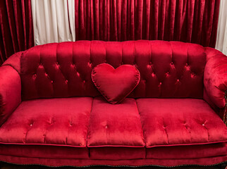 A red velvet couch with a heart shaped pillow on top of it