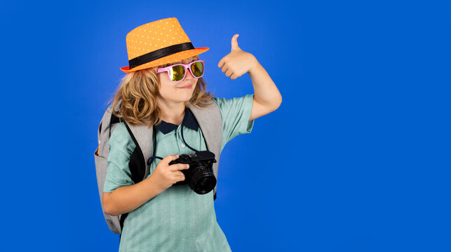 Child traveler with camera and backpack isolated on studio background. Tourist kid boy. Portrait of child travel with travel bag. Travel, adventure, vacation.