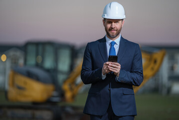 Architect at a construction site. Architect man in helmet and suit at modern home building construction. Architect with a safety vest and suit. Confident architect standing at house background.