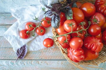 Ripe red cherry tomatoes in a wicker basket on a wooden background.