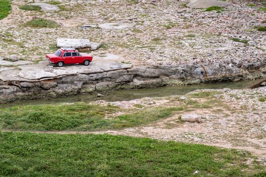 Old Fial 125 car on a bank of canal in rocky shore in Havana, Cuba