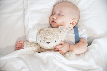 Portrait of a sleeping little child boy on a white pillow in a white bed on a white bed with a teddy bear toy