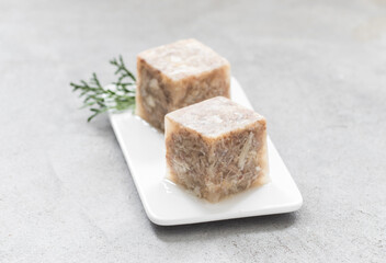 Aspic. Jellied meat in the shape of a cube. On a plate. Light grey background. Close up
