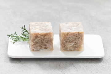 Aspic. Cold appetizer. Chicken jellied meat in the shape of a cube. On a plate. Light grey background. Close up