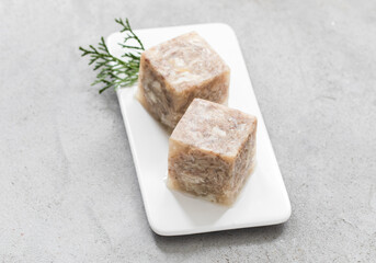 Cold appetizer. Chicken jelly in the shape of a cube. On a plate. Light grey background. Close-up