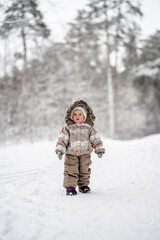 Fototapeta na wymiar Little baby child in a warm jumpsuit walks in a snowy winter forest