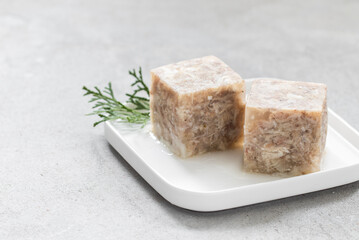 Chicken jelly in the shape of a cube. On a plate. Light grey background. Copy space