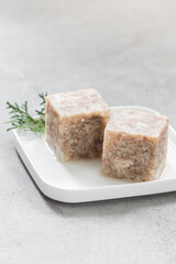 Chicken jelly in the shape of a cube. On a plate. Light grey background. Close-up