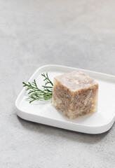 Meat jelly in the shape of a cube. On a plate. Light grey background. Copy space