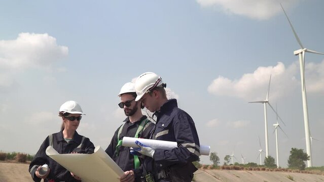 Engineers man and woman inspecting construction of WIND TURBINE FARM. WIND TURBINE with an energy storage system operated by Super Energy Corporation. Workers Meeting to check AROUND THE AREA.