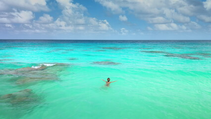 Fototapeta na wymiar Woman swimming on waves in open sea coral reef. Blue water, tropical exotic island. Outdoor lifestyle travel on summer holiday vacation. Panoramic drone view