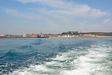 Fototapeta premium View from a boat in the sea to the old city on the shore on the horizon. Foamy waves spread from the boat