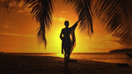 Bright color sunset over tropical island beach landscape. Woman silhouette in long shirt playing...
