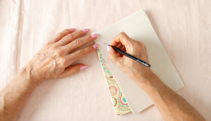Senior adult latin woman writing on old paper. Flatlay, closed angle, close-up.