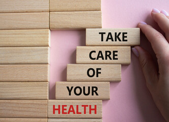 Health symbol. Wooden blocks with words Take Care of your Health. Doctor hand. Beautiful pink...