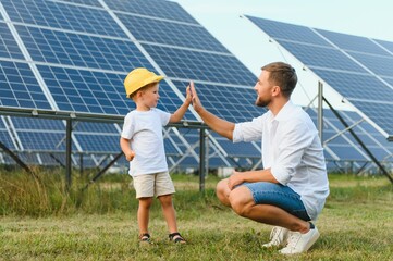 Happy father and his little son are walking near the solar panels. The concept of green energy.