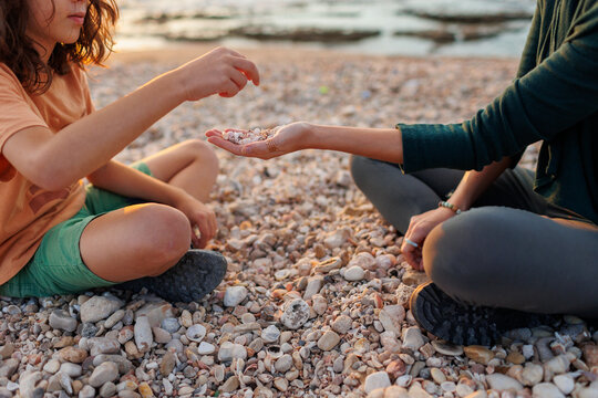 child collects shells and pebbles on a sandy beach with a caring, kind and beautiful mother in a hat on vacation. Family having fun on the beach collecting shells.