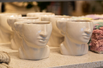 Unique ceramic face-shaped pots or vases on a shelf, with a glossy finish and subtle details, evoking an artistic and modern aesthetic